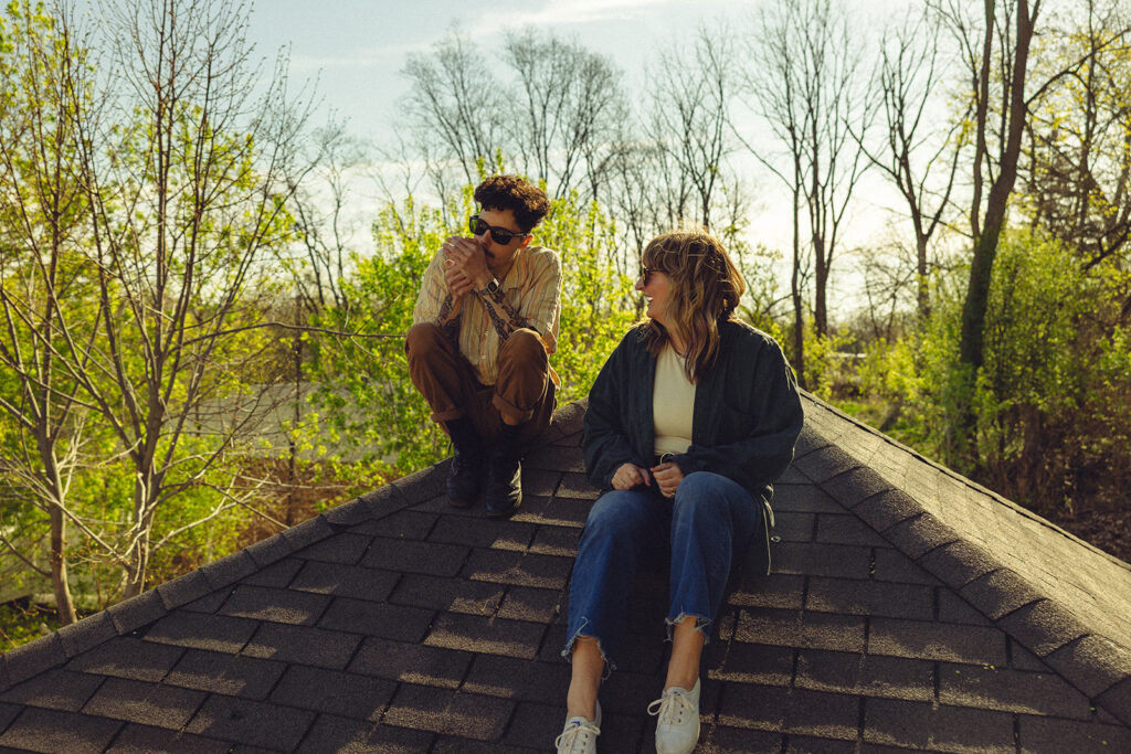 A newly engaged couple are seated on the roof of their home during engagement photos with a West Michigan photographer