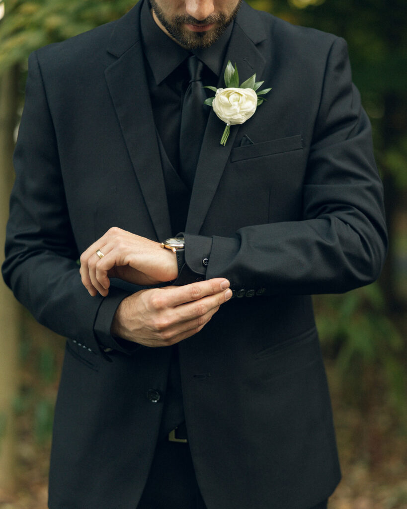 A groom wearing all black adjusts his cufflink in a photo taken at one of outdoor michigan wedding venues