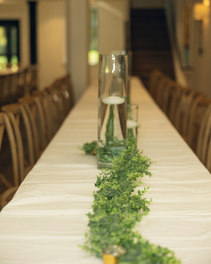 Table decor consisting of greenery and floating candles in hurricane  vases is photographed at a venue for small weddings in michigan