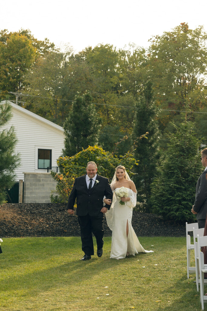 A bride is escorted down the aisle by her father at an outdoor wedding in West Michigan 