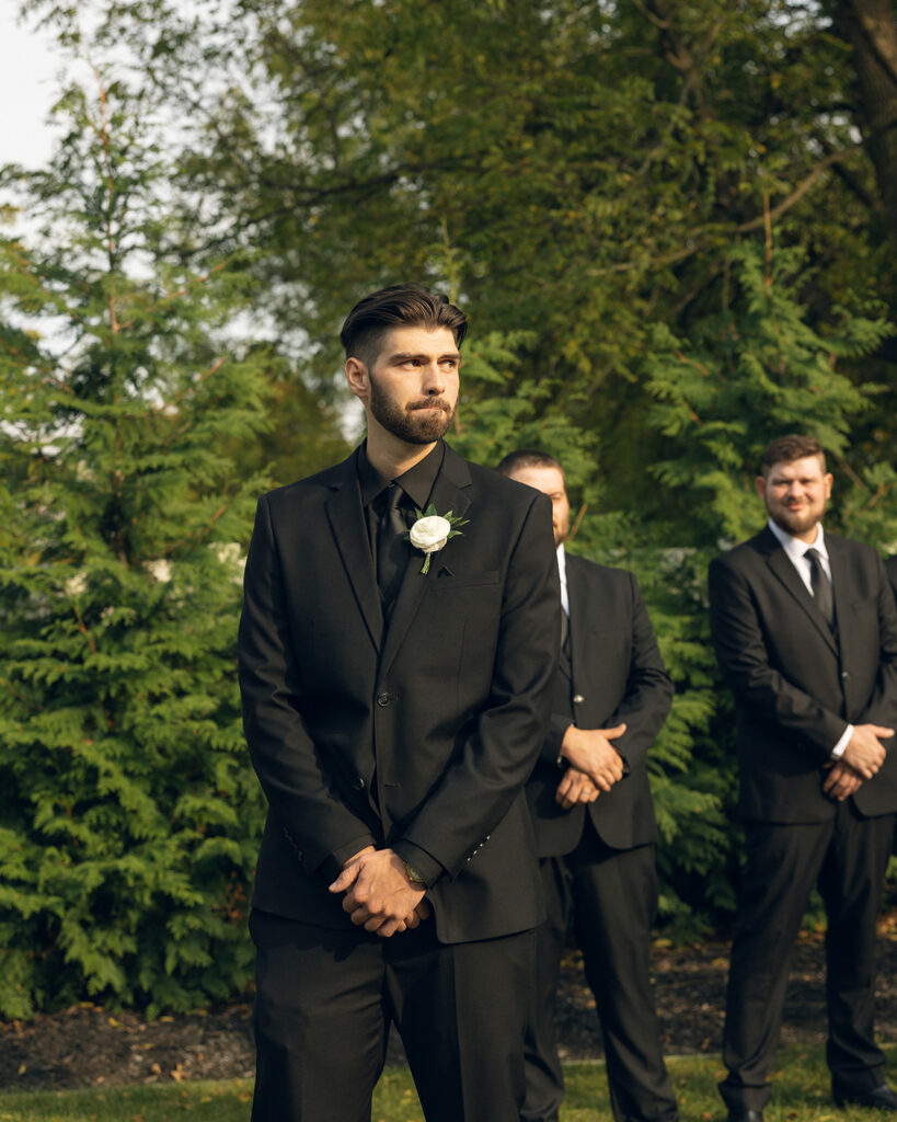 A groom in a black suit is photographed at a Michigan wedding venue 