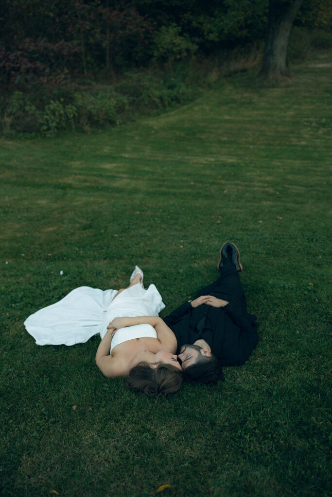 Newlyweds lie in the grass in their wedding attire at a Michigan wedding venue