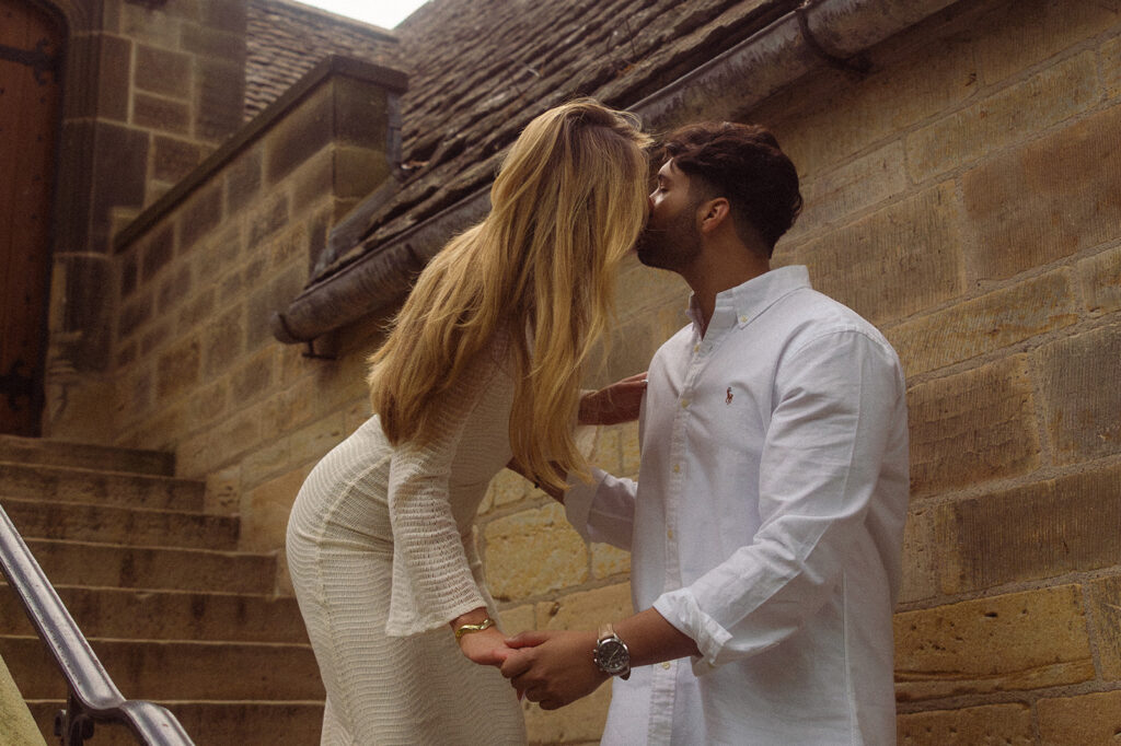 An engaged couple in Michigan share a kiss in a stairwell during an engagement session with a grosse pointe photographer