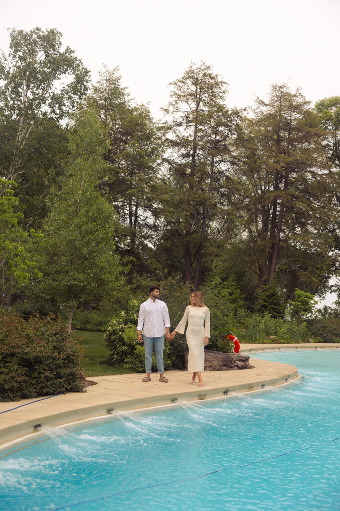 An engaged Michigan couple walk hand in hand next to the pool at the Ford Mansion in Grosse Pointe during their engagement photos with grosse pointe photographer, Anika B Photography
