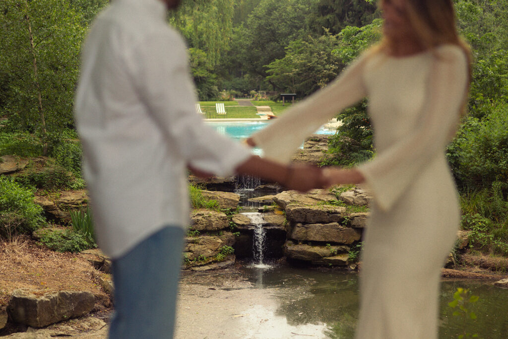 An engaged couple is blurry in the foreground while the pool & grotto at the Ford Mansion Grosse Pointe is in focus in the background in this engagement photo 