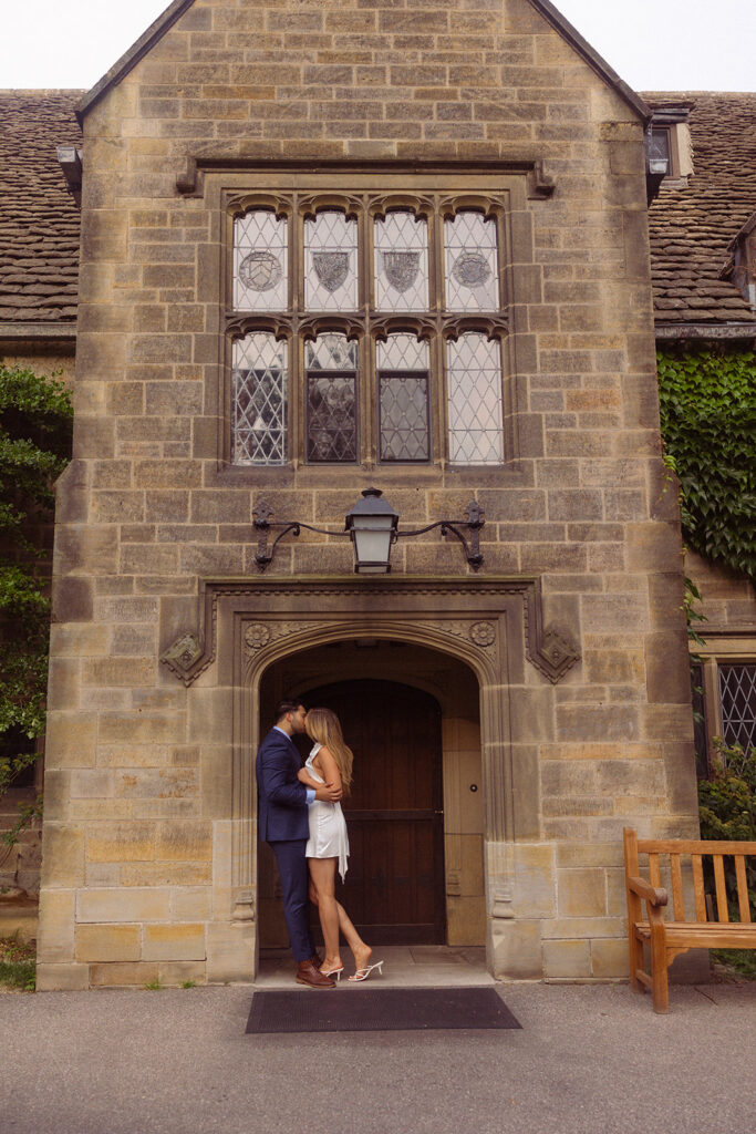 A woman in a white dress leans in for a kiss from her fiance during an engagement session at Ford Mansion Grosse Pointe 