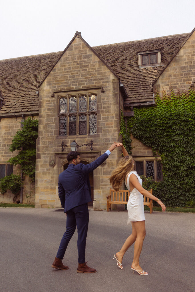 An engaged couple holds hands and twirls in front of the Ford House in Grosse Pointe MI 