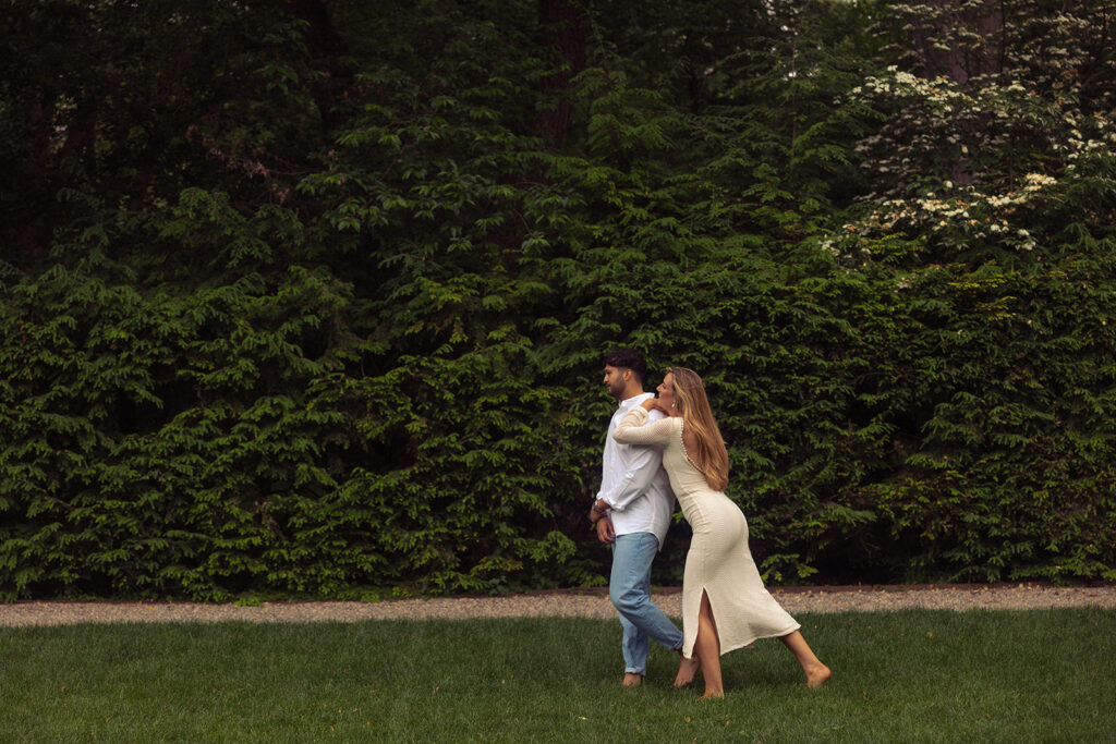 A woman wearing a long cream dress leans against her fiance during an engagement session with grosse pointe photographer, Anika B Photography 
