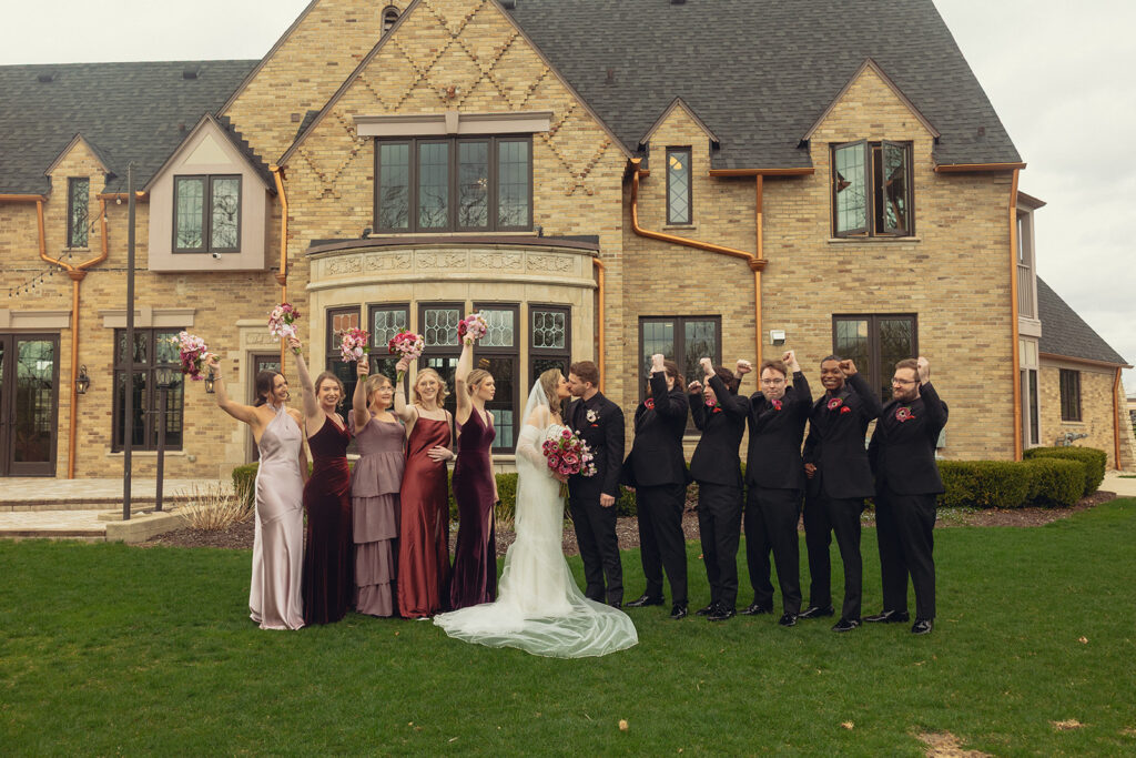 A bridal party wearing deep shades of purple and the groomsmen in black celebrate Michigan newlyweds following their wedding ceremony grand rapids mi