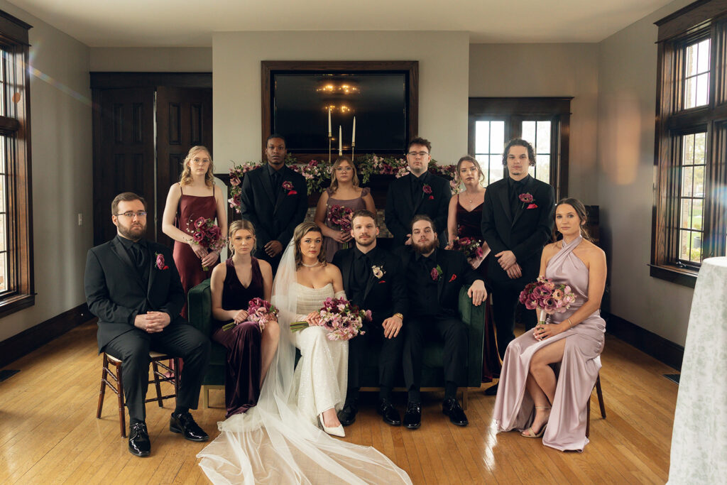 Newlyweds are seated on a green velvet couch with their bridal party and family for a royal family inspired bridal portrait following their wedding at Venue3Two