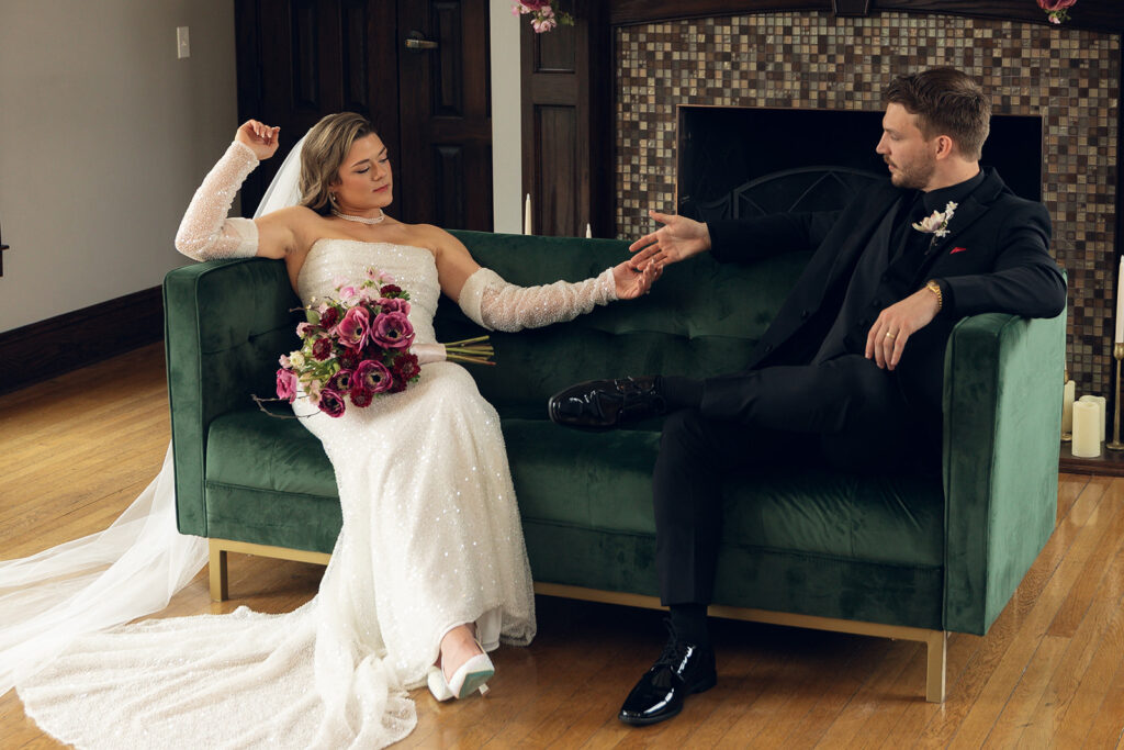 Newlyweds hold hands on a green velvet couch in their wedding attire following their ceremony at all inclusive wedding venues in michigan, Venue3Two