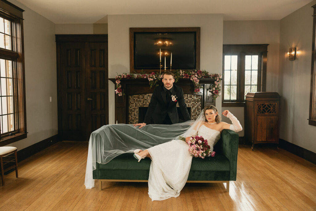 A Michigan couple poses in a suite at Venue3Two in their wedding attire on a green velvet couch after their Grand Rapids ceremony