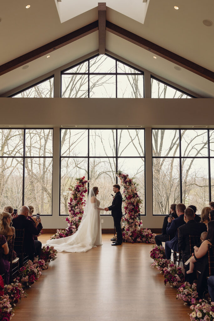 Newlyweds stand hand in hand beneath a floral arch in a photo taken by Michigan wedding photographer, Anika B Photography