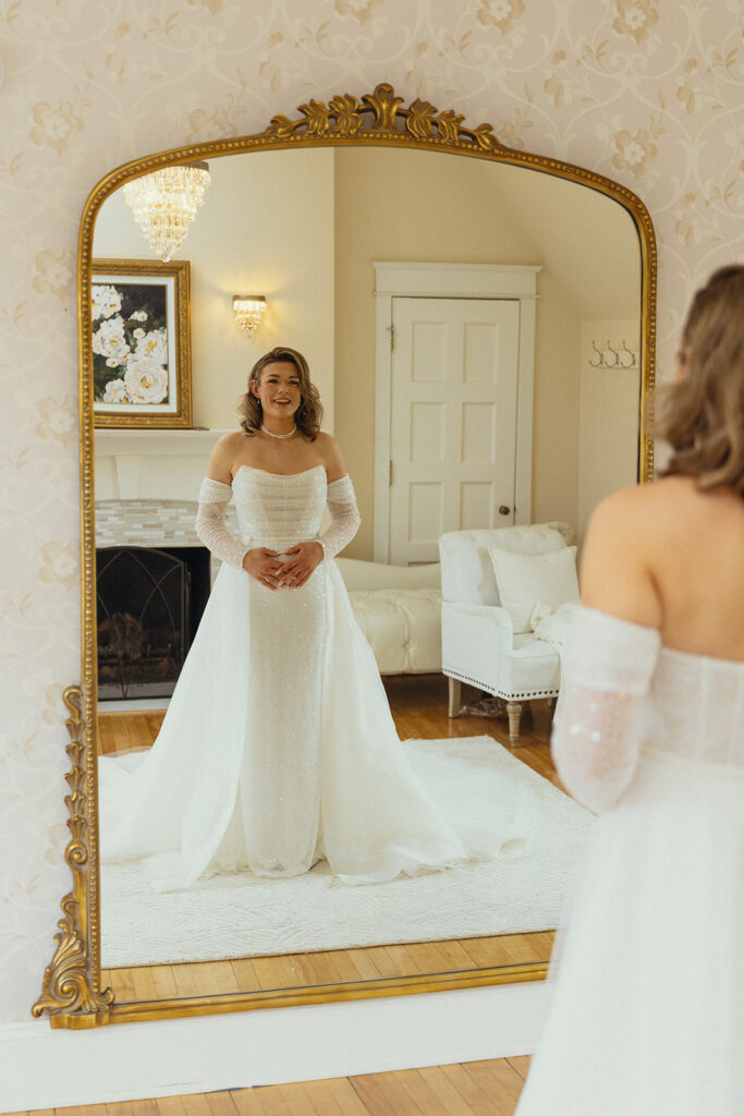 A bride in a strapless white gown stands before an ornate mirror in an on-site bridal suite at Venue3Two, an event space grand rapids mi