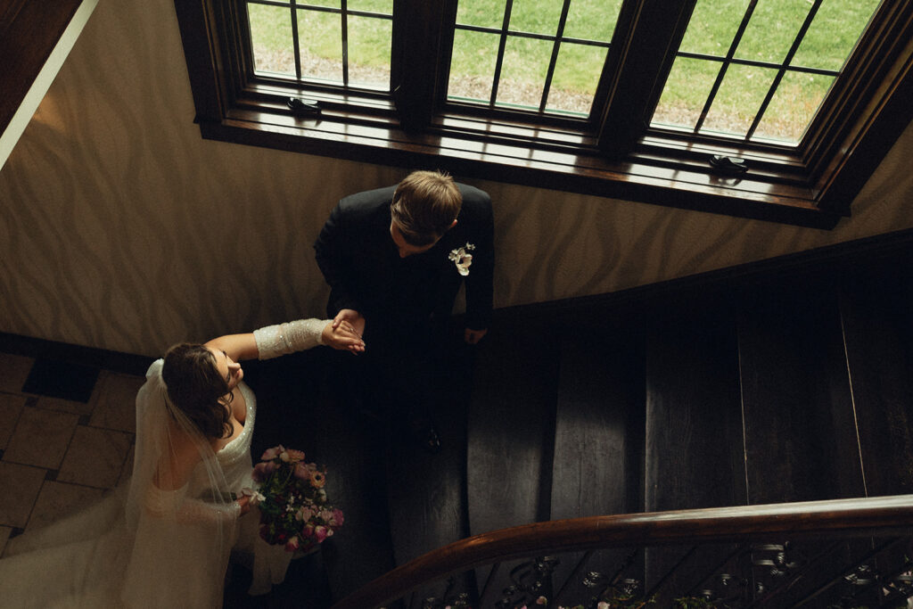 Newlyweds walk hand-in-hand up a staircase at the event space grand rapids mi where they held their luxe wedding