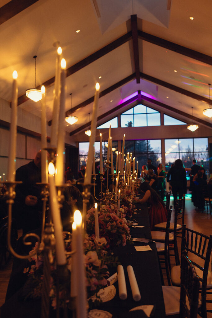 Tapered candles are lit amongst florals at a wedding reception at Venue3Two