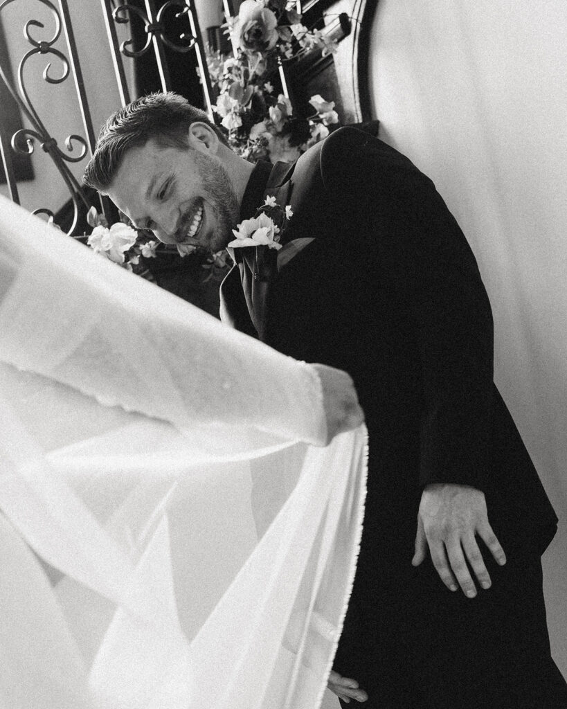 A black and white photo depicts a groom smiling during a first look at his bride before their wedding ceremony grand rapids mi